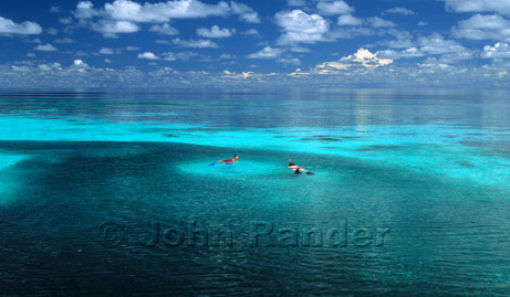 Two swimmers surrounded by a school of fish in the Maldives